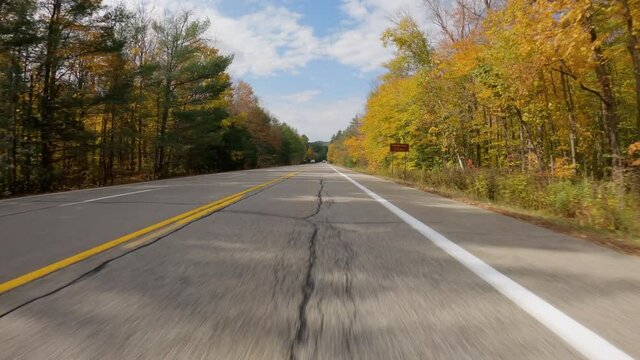 POV Driving a car on asphalt road with colorful trees in autumn scenery. Clear blue sky with white clouds