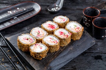 tempura roll with fish, tobiko, creamy sauce and cucumber. black wooden background and decor.