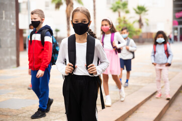 Portrait of tweenager girl in protective mask with backpack going to school lessons on warm autumn day. New lifestyle during coronavirus pandemic.
