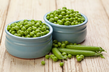 Green peas in blue bowls on white wooden background