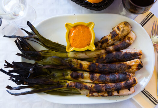 Top view of grilled calcots traditionally served with romesco sauce and red wine in restaurant. National Catalan winter dish