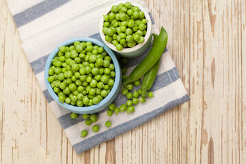 Green peas in bowls on white wooden background