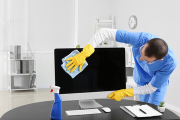 Male janitor cleaning computer in office