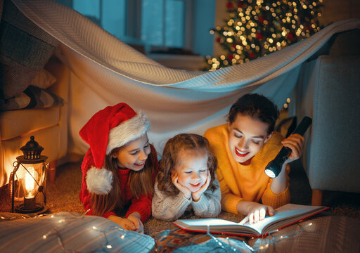 mother reading book to daughters near Christmas tree
