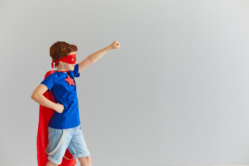 Little smiling boy in a superhero costume with a red cloak and glasses is ready for adventure.