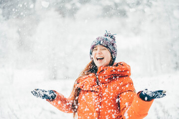 Young smiling girl in a orange coat throwing up snow in a winter forest.