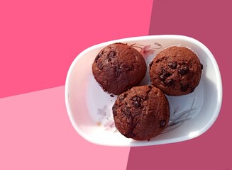 Chocolate chip sprinkled cup cakes in white paper on a plate. Top view. Selective focus. Colourful mauve pale pink background. food, snack for party, celebration purpose.