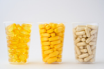 sport dietary nutrition concept of three plastic cups with pills softgels omega3 capsule vitamins tablets on white background with copyspace