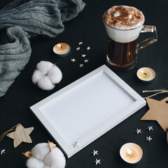 Obraz na płótnie Canvas Photo frame, coffee cup, candles, sweater on a black background. Cozy winter concept with copy space.
