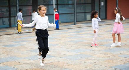 Happy schoolgirl jumping game by rubber band, kids friends on background