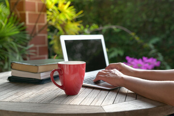 Woman typing on computer laptop with books on table, Focus on red cup.