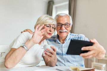 Senior couple smiling and looking at the same tablet hugged. Indoor, at home concept. Mature and retired man and woman using technology - lockdown and quarantine lifestyle