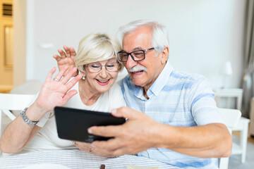 Senior couple smiling and looking at the same tablet hugged. Indoor, at home concept. Mature and retired man and woman using technology - lockdown and quarantine lifestyle