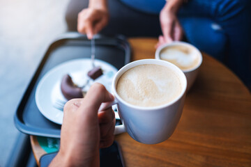 Closeup image of two people clink white coffee mugs in cafe