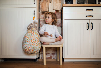 Portrait of mall girl sitting indoors in kitchen at home.