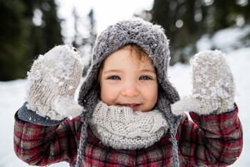 Front view portrait of cheerful small girl standing in winter nature, looking at camera.