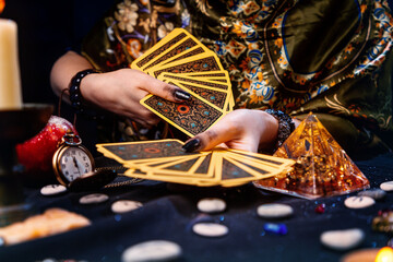 Astrology and esotericism. A fortune teller holds a fan of Tarot cards. On the table are runes and talismans. Close-up of hands