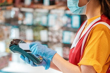 Portrait of an female worker in a uniform with a medical mask on her face and rubber gloves making an online payment. Hands close up. Side view. Concept of online payments by Bank cards