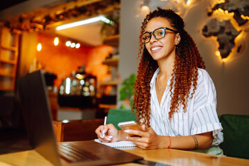 Young woman working online on laptop computer sitting in cafe. Smiling student wear wireless headphone study online, listen lecture, watch webinar, distant education. Freelancer working outside office