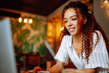 Young woman working online on laptop computer sitting in cafe. Smiling student wear wireless headphone study online, listen lecture, watch webinar, distant education. Freelancer working outside office