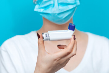 Bronchial asthma. A female doctor in a medical mask, holding an inhaler in front of her. The hand with the medicine close-up. Blue background