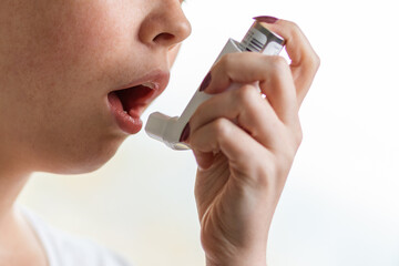 Asthma. The woman brings the inhaler to her mouth. Close-up of the hand and lower half of the face....