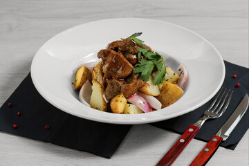 Stewed lamb fillet with new potatoes and red onion is on the wooden background with fork and knife.