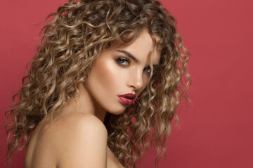 Fashion portrait of nice young woman with makeup and curly hairstyle on red background