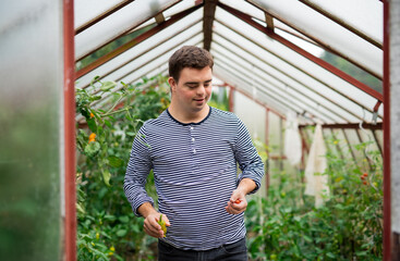 Down syndrome adult man walking in greenhouse, gardening concept.