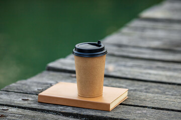 
paper Cup of coffee and a book on a wooden bridge by the river
