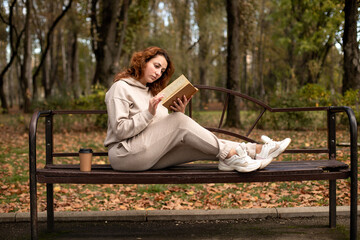 a young beautiful girl is sitting on a bench in an autumn Park and reading a book