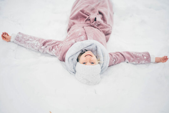 Happy young woman lying on snow and making snow angel figure.