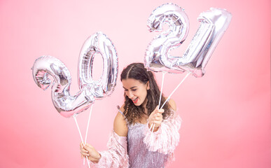 Girl on a pink background with silver balloons from the numbers 2021 in her hands