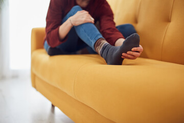 Woman with feet intense pain sitting on a couch at home.