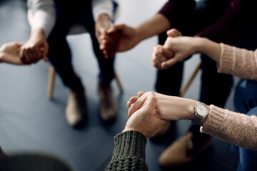 Close-up of attenders of group therapy holding hands during the meeting.