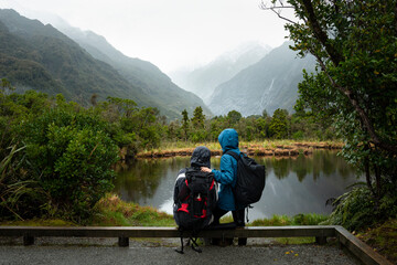 Couple enjoying the view of Franz Josef Glacier valley reflected in the Peter’s Pool, South Island, New Zealand