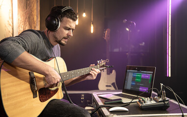 European man plays the guitar while recording a track in a music studio.