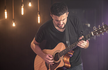 Guitarist playing acoustic guitar against blurred dark background at concert.