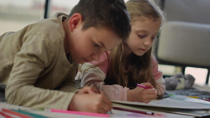 Boy girl coloring pictures on floor. Cute siblings painting in sketchbooks home