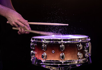 Drum sticks hitting snare drum with splashing water on black background under studio lighting.
