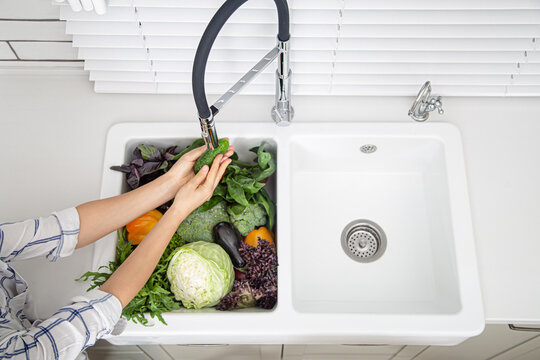 Female hands washing vegetables in the kitchen sink of modern kitchen top view.