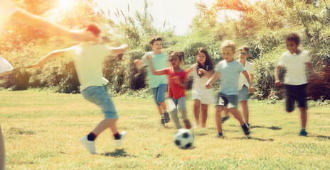 Group of happy kids are running and playing football in park at summer day