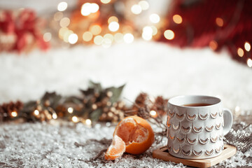 Cozy winter background with a beautiful cup and tangerine on a blurred background with bokeh.
