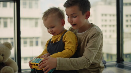 Obraz premium Younger brother sitting in older laps on carpet. Children playing toy car.