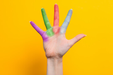 A woman's hand with multicolored fingers spread out. Yellow background. The concept of the world day of protection of children