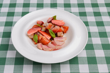Meat in sweet and sour sauce with strawberries. Served in a white plate over green plaid tablecloth.