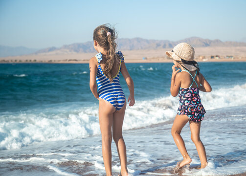 Two little girls play along the beach by the sea.