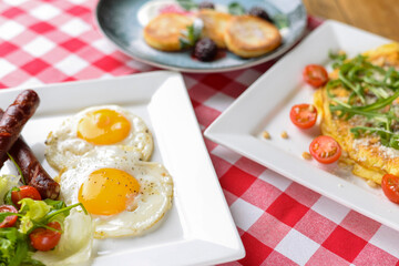 Breakfast with salad, fried egg and sausages served in white plate over red plate tablecloth.