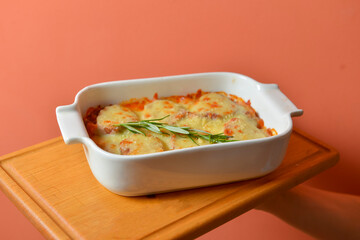 Italian casserole with cheese and vegetables on hand over pastel colored background. Delicious Italian cuisine concept.