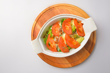 Baked mixed vegetable casserole with broccoli and tomatoes. Served in a white pot over white background.